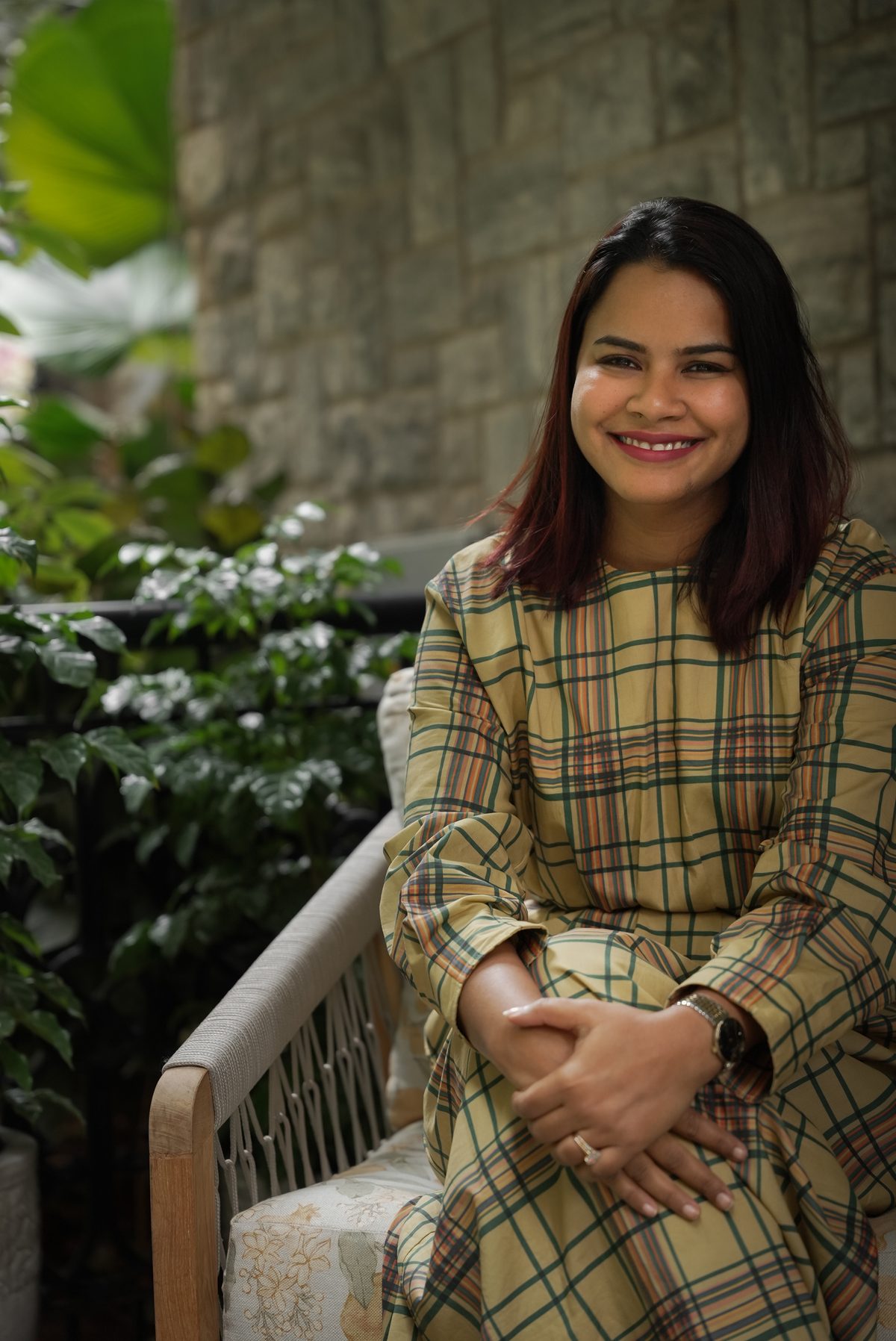 Monica, founder and lead designer of Spaces by Monica, seated on a rattan bench surrounded by greenery